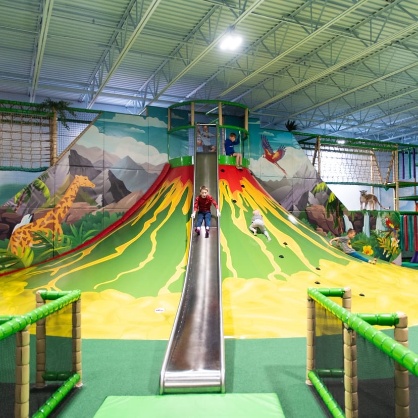 Children playing and sliding down a large volcano-themed slide at an indoor playground