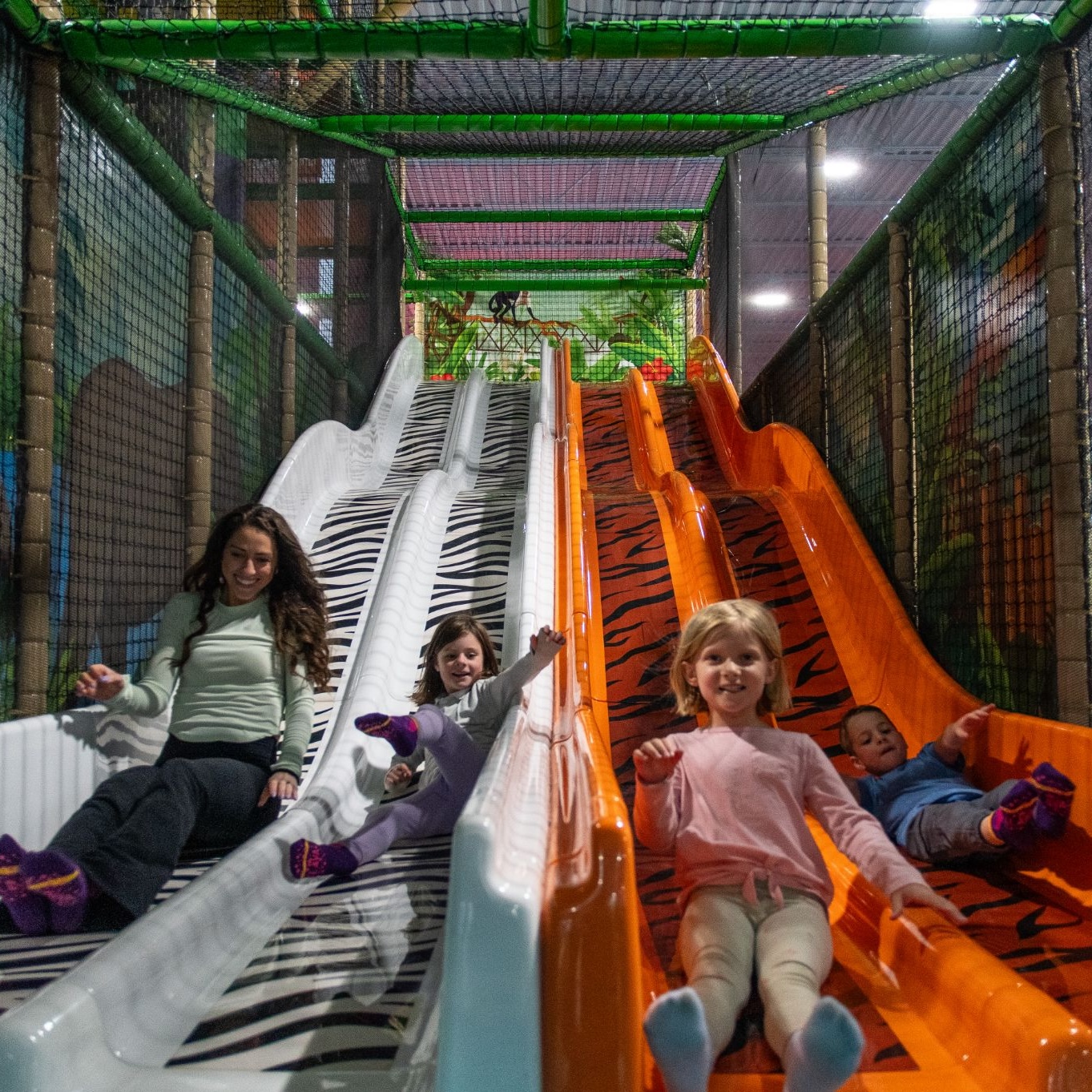 Children and an adult sliding down colorful zebra and tiger print slides in an indoor playground