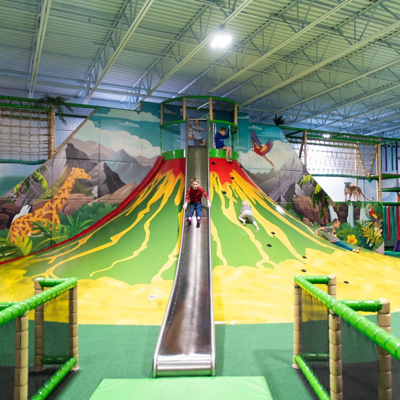 Children playing and sliding down a large volcano-themed slide at an indoor playground